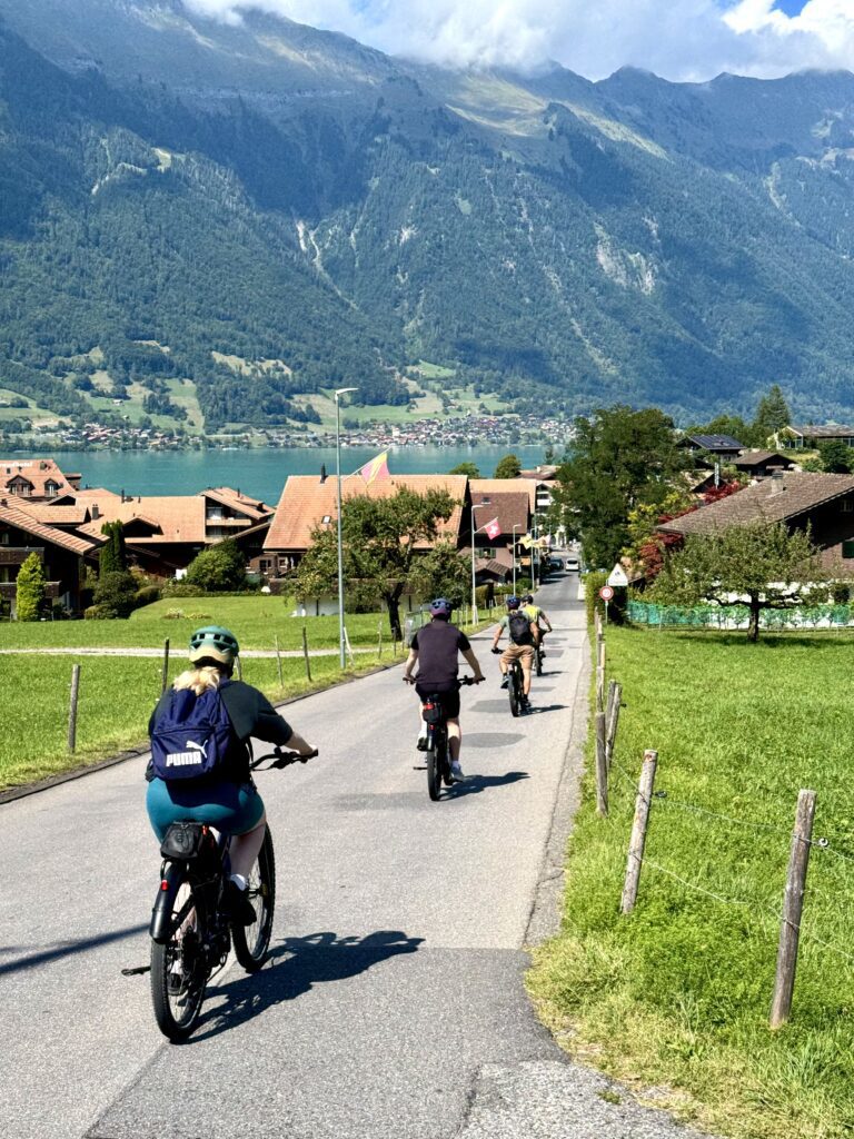 Cyclists riding e-bikes through the picturesque village of Iseltwald on Lake Brienz