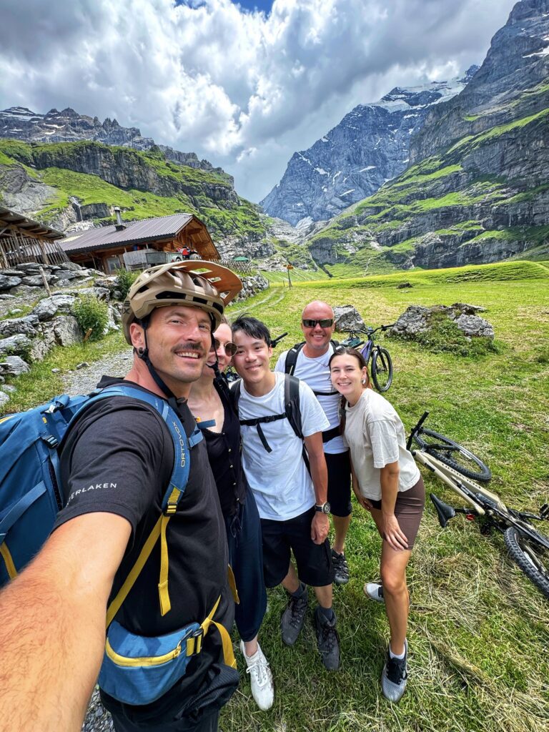 Group of cyclists on the Griesalp UNESCO E-bike tour in Kiental, surrounded by dramatic Swiss Alps cliffs and alpine scenery.