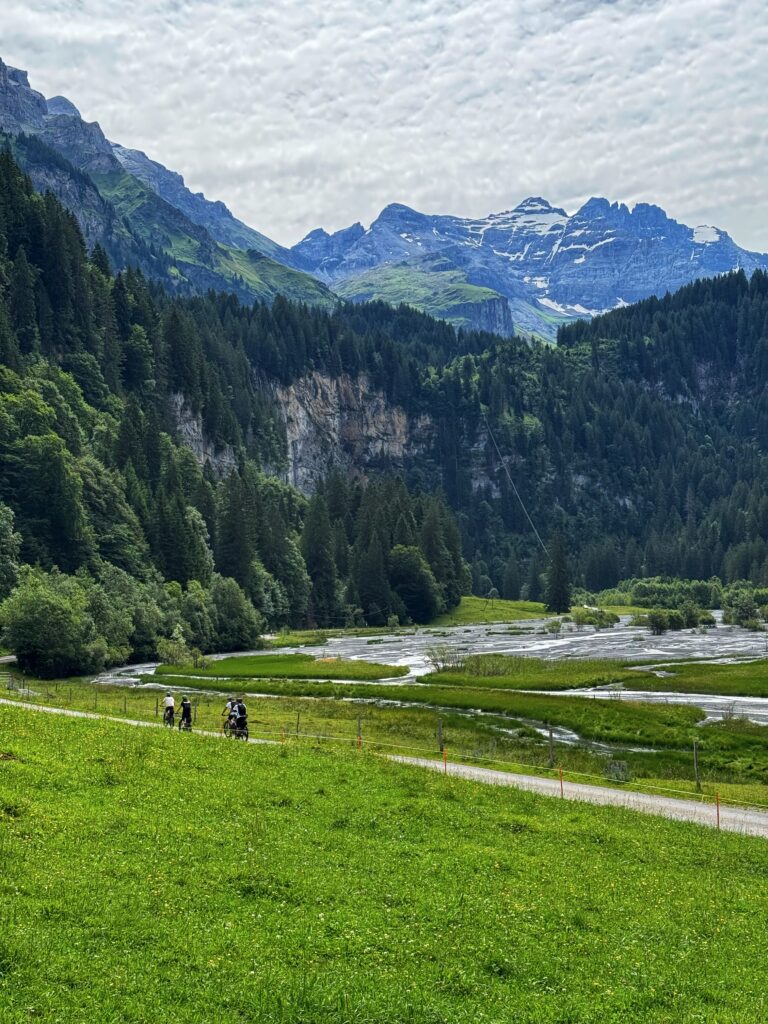Cyclists on the Griesalp UNESCO e-bike tour in the Kiental valley near Interlaken, with Swiss Alps peaks and alpine wetlands in the background.